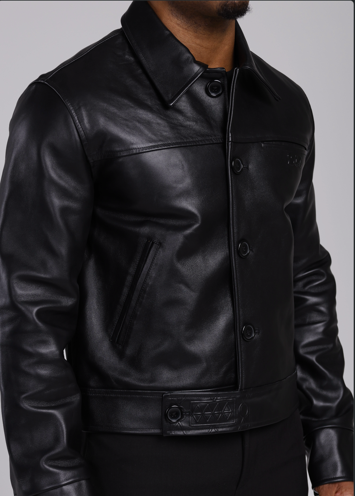 Man wearing a the 244 angels at heart black cowhide leather jacket and pants on a grey background. side viewhalf-body shot, jacket closed
