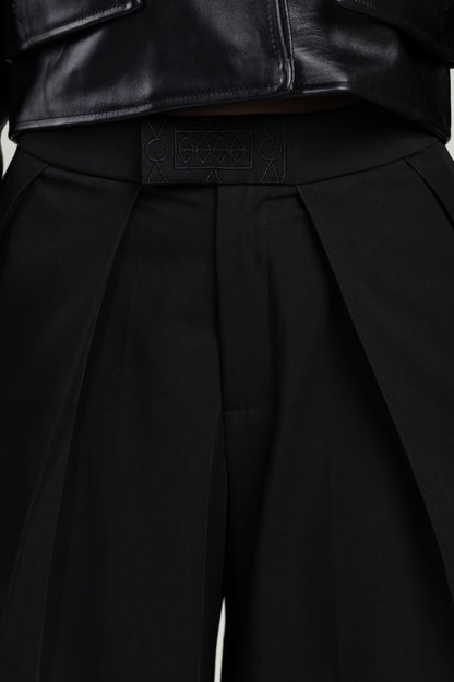Close-up of a black pleated pants with an embroidered brand logo on a white background
